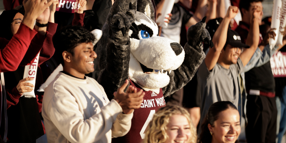 The Husky mascot cheers in the stands with students
