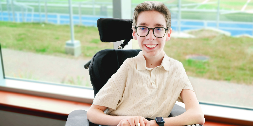 Van is a young white man who uses a power wheelchair. He has short brown hair and glasses.