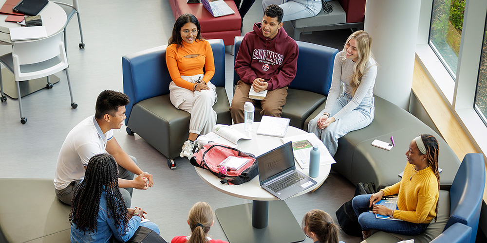 A group of students sit on curved benches indoors